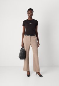 T-shirt nera a maniche corte con testo bianco, pantaloni beige a righe a vita alta, décolleté nere con punta appuntita e una borsa nera con motivo.