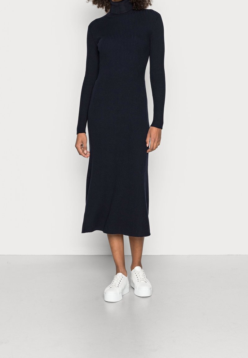 Laivastonsininen ribbed-kudottu mekko korkealla pääntiellä, pitkät hihat ja vartalonmyötäinen siluetti, yhdistetty valkoiseen korokepohjaisten tennareiden kanssa.