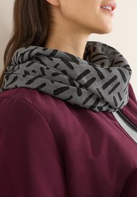 Geluidsloop in grijze stof met een zwart abstract patroon, gedragen over een bordeauxrode jas. Soepele textuur en casual ontwerp.