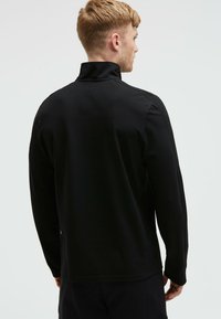 Schwarzer Pullover mit langen Ärmeln und hohem Kragen, der über eine glatte Oberfläche und ein schlankes Design verfügt. Die Rückansicht zeigt dezente Nähte und eine lockere Passform.