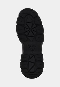 Suola di scarpa in gomma nera con una superficie testurizzata, caratterizzata da un motivo di battistrada geometrico e un logo triangolare al centro.