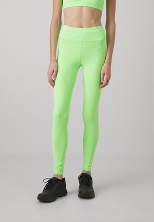 Neongröna leggings i elastiskt material, med hög midja och åtsittande design. Svarta träningsskor kompletterar outfiten.