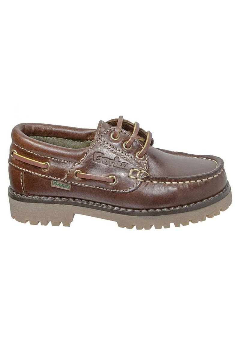 Zapato náutico de cuero marrón con dos ojales, costuras contrastantes y una suela de goma texturizada. Presenta un logotipo y un detalle de lazada decorativa.