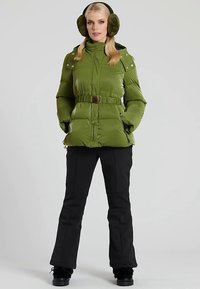 Zielona kurtka puchowa z paskiem, kieszeniami na zamek i wysokim kołnierzem, zestawiona z czarnymi spodniami i czarnymi butami. Miękki materiał i uporządkowany krój.