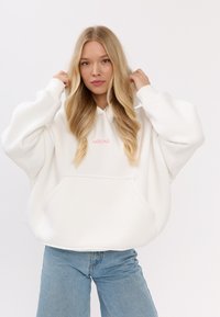 Oversized witte hoodie met een voorzak, voorzien van een klein roze logo. Soepele textuur, capuchon met trekkoord en verlaagde schoudernaden.
