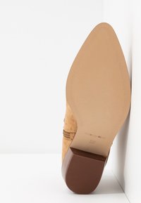 Světlý semišový lodička na vysokém podpatku s špičatou špičkou a dřevěným podpatkem; hladká podrá�žka zdobená švy a označením "MADE IN SPAIN" a velikostí "37".