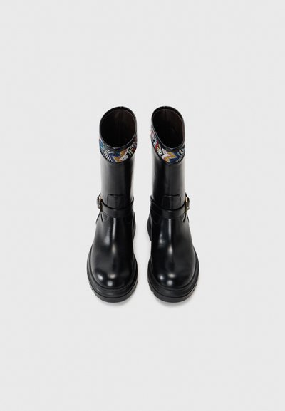 Black leather ankle boots with a textured fabric cuff in multicolor patterns, featuring a side buckle accent and a chunky sole.