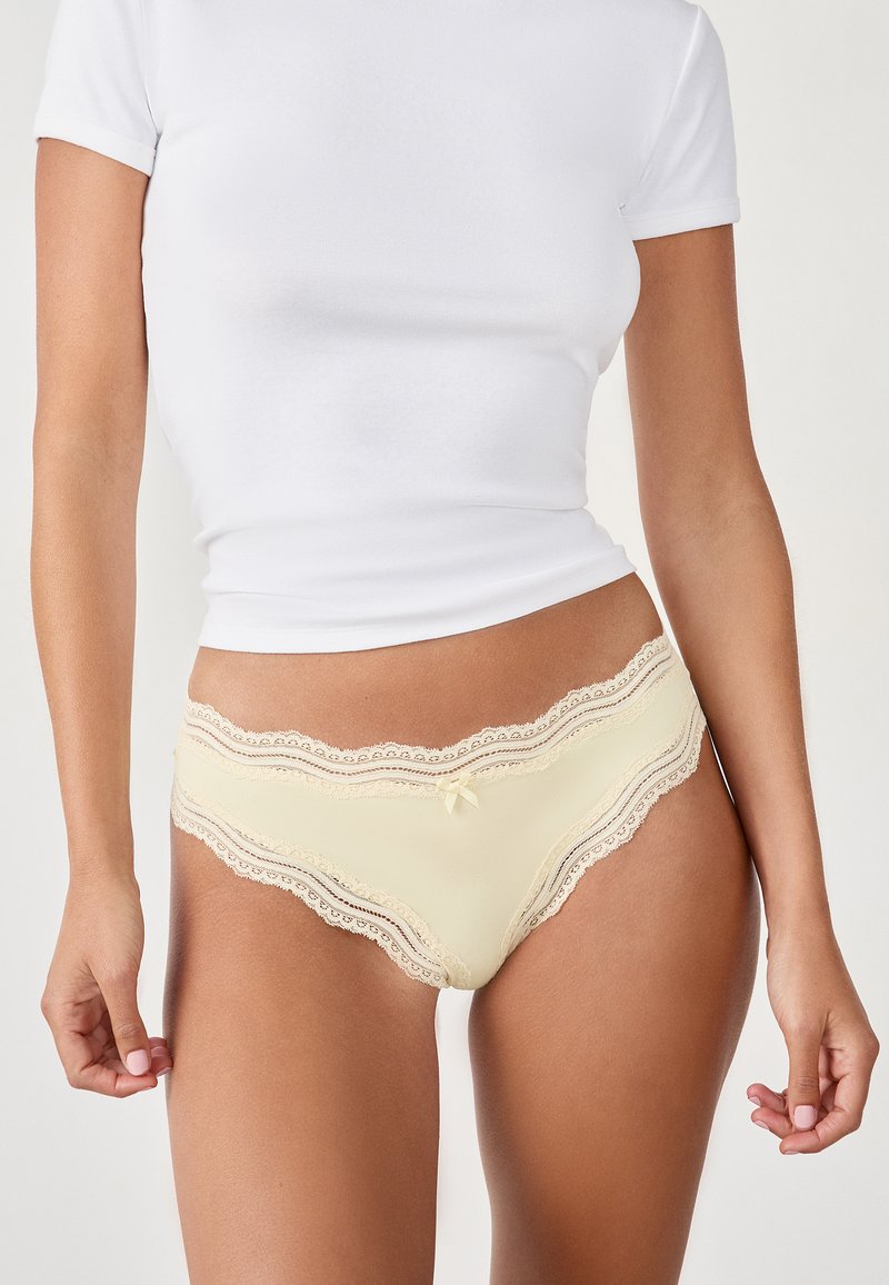 Culotte légère jaune pâle bordée de dentelle avec un bord festonné et un petit nœud. Fabriquée en tissu doux, mettant en valeur des accents en dentelle délicats.