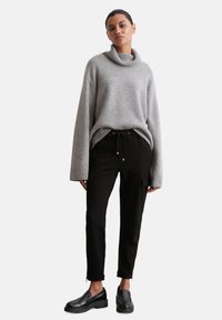 Grijze gebreide coltrui met een losse pasvorm en ribbelmanchetten, gecombineerd met zwarte tapered broek met zakken en ritsaccenten. Zwarte loafers.