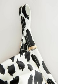 Svart och vit mönstrad rem av mjukt tyg, med en guldfärgad metallaccent och vita sömmande detaljer för hållbarhet.