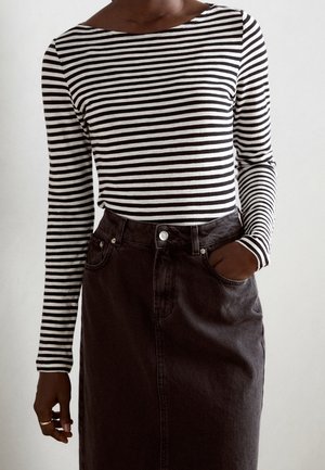 Maglietta a righe a maniche lunghe bianca e nera con scollo a barca, abbinata a una gonna di jeans scuri con tasca frontale e chiusura a bottoni.