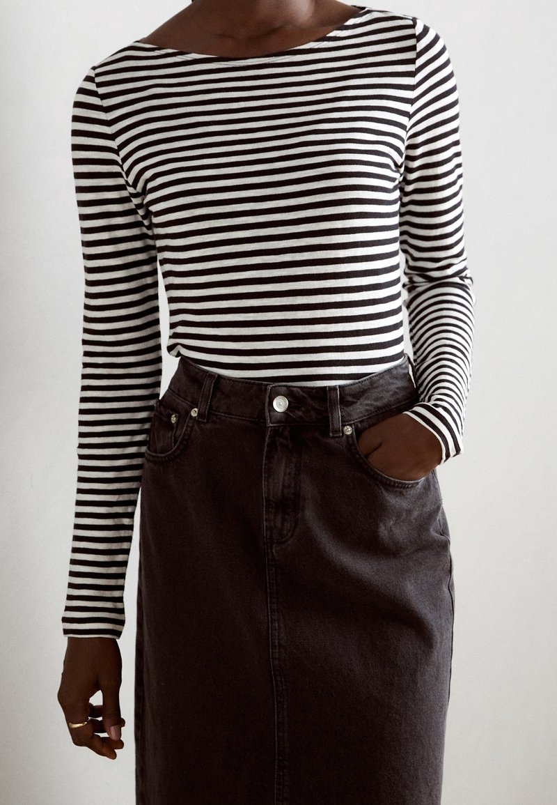 Gestreiftes Langarmoberteil in Schwarz und Weiß mit einem Schiffsausschnitt, kombiniert mit einem dunkelblauen Denimrock mit einer Fronttasche und Knopfverschluss.