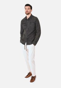 Camicetta button-up grigio scuro con due tasche sul petto, abbinata a pantaloni bianchi e sneakers marroni. Design semplice, texture in cotone.