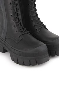 Botas de cuero negras hasta el tobillo con una suela gruesa y texturizada. Cuentan con cordones, una cremallera en el lateral y una superficie lisa.
