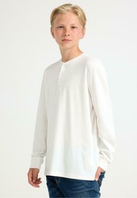 Witte lange mouwen henley-shirt met een ronde hals en een drieknoopsluiting. Zachte textuur en ribbelstof, gecombineerd met donkerblauwe jeans.