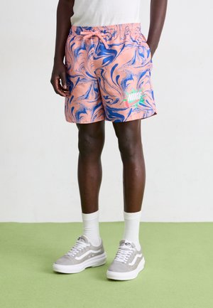 Shorts marbrés roses et bleus avec une taille élastique, ornés d'un logo Nike vert fluo. Portés avec des baskets gris et blanc et des chaussettes blanches.