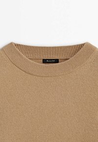 Beige stickad tröja med ribbade ärmslut, mjuk textur och en etikett sydd på insidan av halsen.