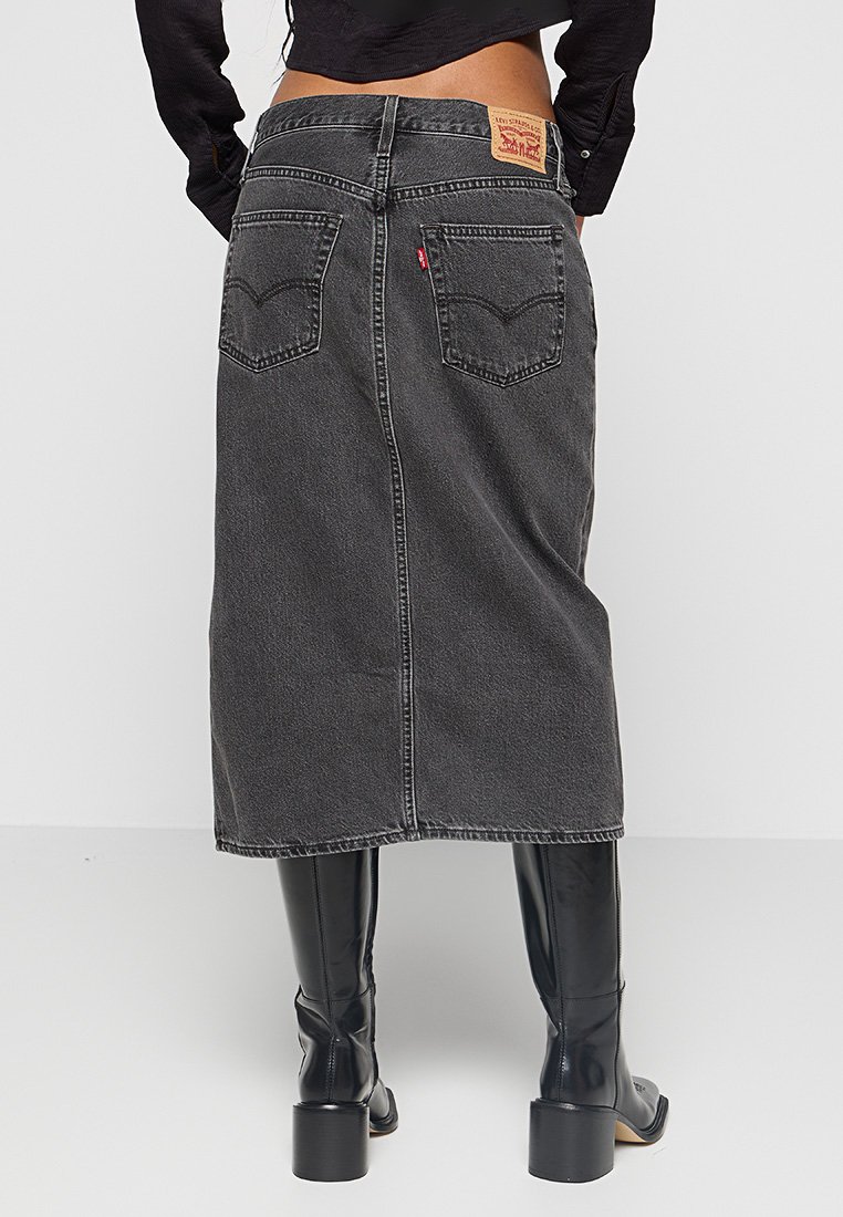 Falda de mezclilla gris oscuro con corte recto, dos bolsillos traseros, una etiqueta de Levi's y un dobladillo que cae por debajo de la rodilla. Llevada con botas hasta la rodilla.