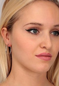 Orecchini a cerchio argentati, capelli biondo chiaro, trucco naturale, pelle liscia e un leggero colore di labbra rosa con eyeliner a ala definito.