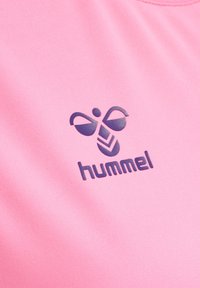 Camiseta deportiva rosa con un tejido texturizado, cuello acanalado y un logotipo morado oscuro con un diseño abstracto y la palabra "hummel."