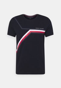 Tmavě modré bavlněné tričko s kulatým výstřihem, které má geometrický design v barvách bílé, červené a šedé, a logo text.