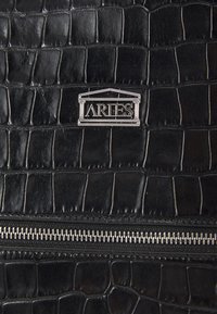 Schwarze Kunstledertasche im Krokodilleder-Look mit einem silbernen Reißverschluss und einem eingeprägten "ARIES"-Logo in einem rechteckigen Rahmen.