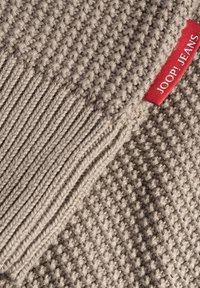 Beige stickad tyg med ett strukturerat mönster; har en ribbad kant och en röd etikett med texten "JOOP! JEANS."