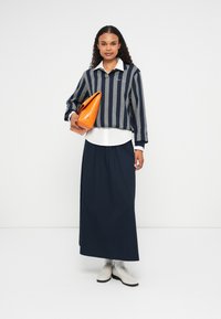 Stripet navy og grå genser med krage over en hvit skjorte, kombinert med et langt navy skjørt og en oransje clutch. Modellen har på seg grå ankelstøvler.