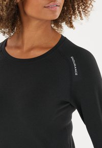 Schwarzes, langärmeliges Sportoberteil mit strukturiertem Ribbelmuster, runder Ausschnitt und "ENDURANCE"-Logo auf der Schulter. Glatte Stoffoberfläche.
