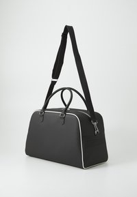Borsa duffel nera con due manici superiori, tracolla regolabile, piping bianco e dettagli perforati su un lato. Materiale sintetico liscio.