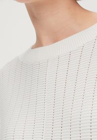 Pull blanc en maille présentant une texture côtelée avec des rayures verticales et un large décolleté. Confectionné dans un matériau léger avec une finition douce.