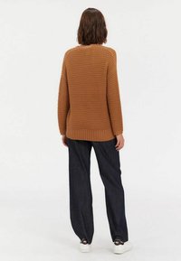 Pull en maille marron avec un motif texturé, côtes aux poignets et à l'ourlet, associé à un jean ample bleu marine et des baskets blanches.
