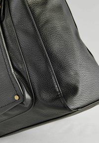 Schwarze Ledertasche mit strukturiertem Oberflächen, ausgestattet mit goldfarbener Hardware und Nähdetails. Die Form ist strukturiert mit einem gerundeten Boden.