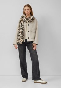 Beige, wollen jack met een boxy fit, grote zakken en donkere, wijde jeans. Geaccentueerd met een gestructureerde luipaardprint sjaal en witte sneakers.