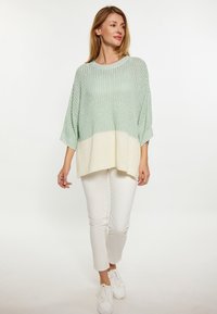 Maglione leggero lavorato a maglia in verde menta e crema, con una vestibilità ampia, maniche larghe e tessuto texturizzato. Abbinato a pantaloni e scarpe bianche.
