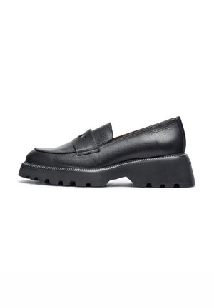 Mocasines de cuero negro con una superficie texturizada, suela de goma gruesa y un destacado detalle de costura frontal. Diseño elegante con un tacón bajo.