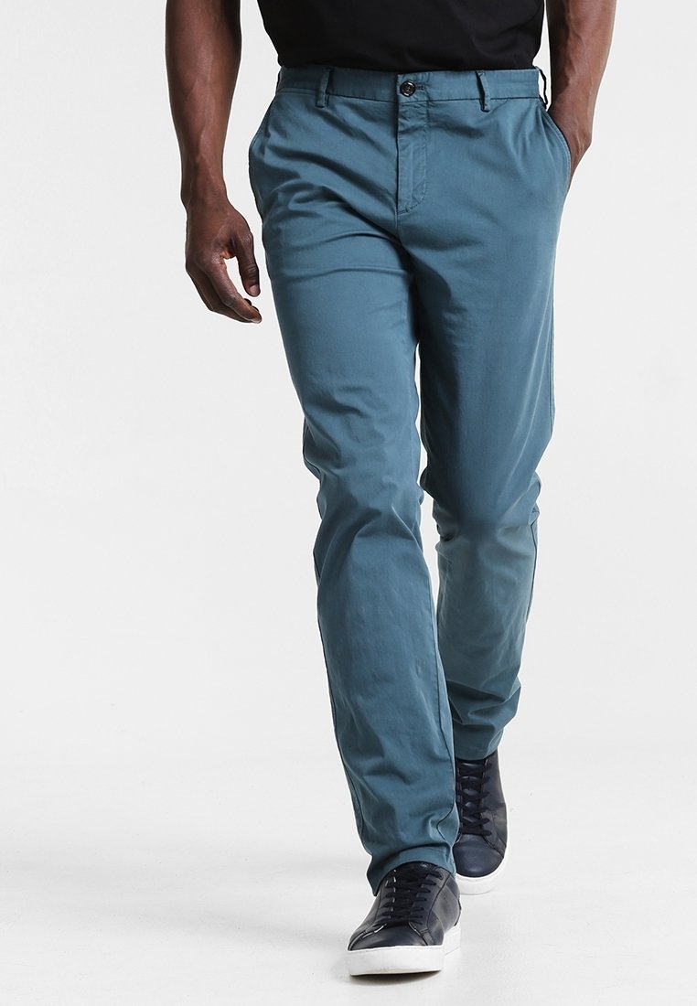 Pantaloni in twill di cotone blu con vestibilità dritta, dotati di tasche laterali, chiusura frontale con bottone e una superficie liscia. Indossati con sneakers scure.