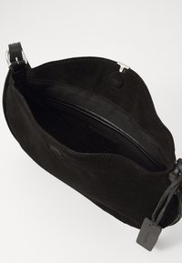 Sac en cuir suéd�é noir à bandoulière avec une fermeture magnétique, ouverture sur le dessus montrant un intérieur doublé et une poche zippée intérieure.