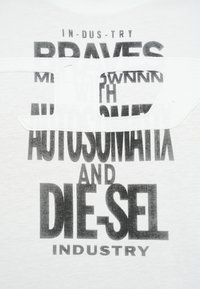 White T-shirt featuring bold black text with varying sizes. Design includes cut-out detail with overlapping letters, creating depth.