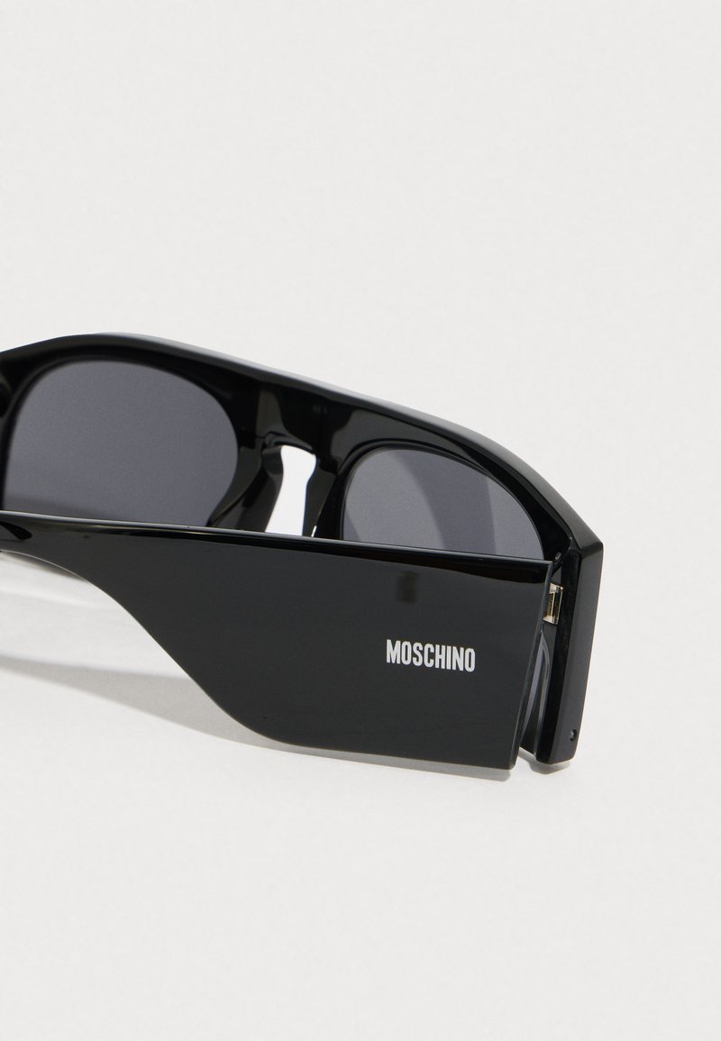 Schwarze Sonnenbrille mit einem schlanken Design, ausgestattet mit dunklen Gläsern, glänzender Oberfläche und "MOSCHINO"-Markenlogo an der Seite.