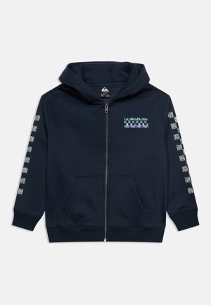Tumši zila rāvējslēdzēja džemperis ar priekšējo kabatu, Quiksilver logotipu un šaha dēļa rakstu krūtīs un gar abām piedurknēm.