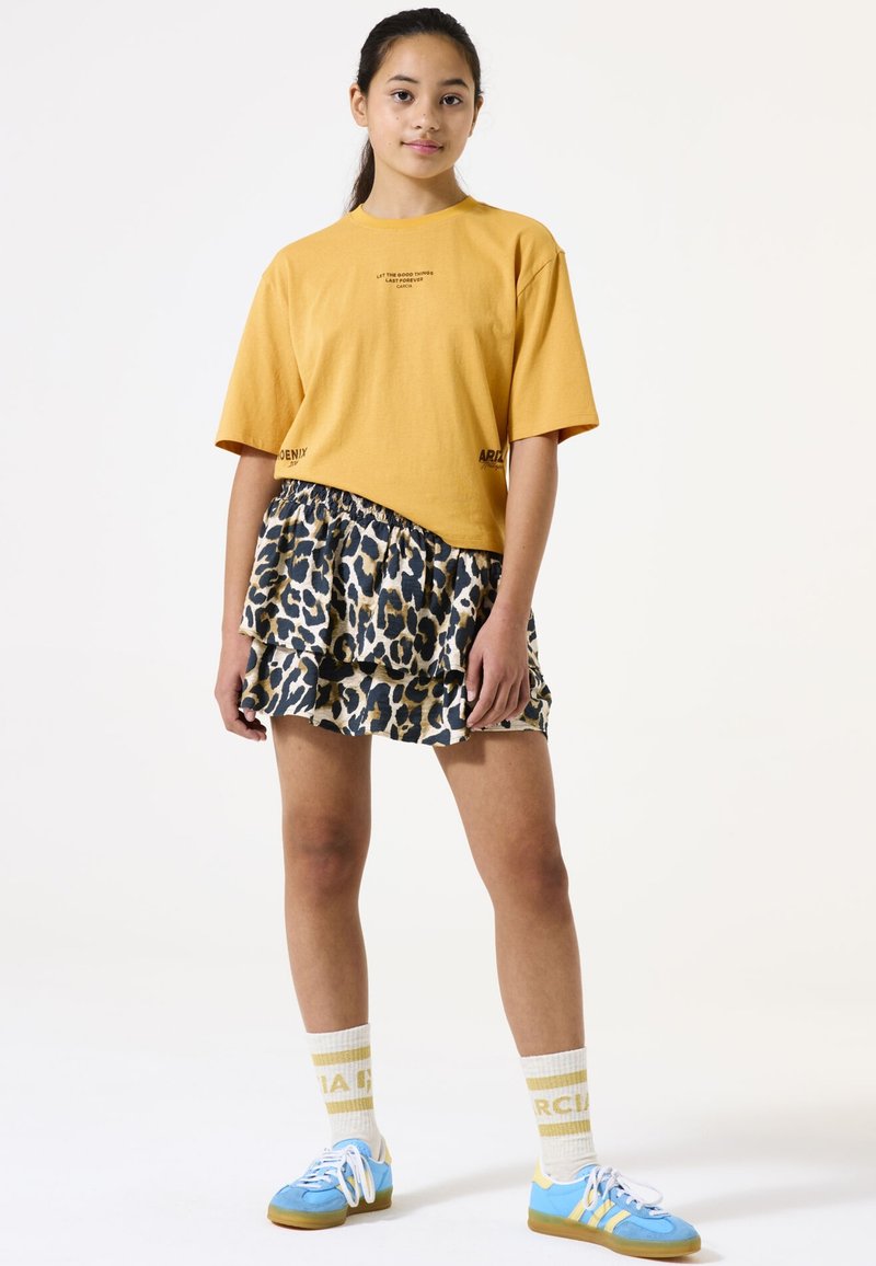 Camiseta amarilla corta con texto impreso, combinada con una falda de leopardo con volantes. Zapatillas deportivas azules y calcetines amarillos a rayas completan el look.
