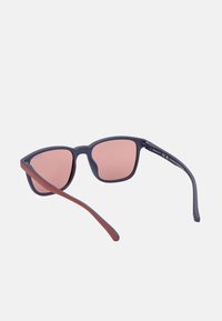 Gafas de sol con un marco mate azul marino, lentes rosas y acentos en burdeos en las patillas. Forma de ojo de gato redondeado con un diseño elegante.
