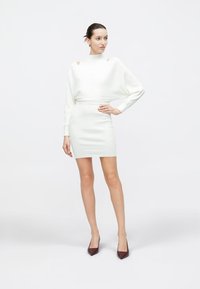 Weißes, leichtes Kleid mit figurbetontem Min Rock und lockerem Pullover-Stil Oberteil. Mit Ausschnitten an den Schultern und gerippter Struktur.