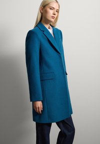 Teal wollen jas met een gestructureerd ontwerp, met een reverskraag, zijzakken en een getailleerde silhouet, gecombineerd met donkere spijkerbroeken.