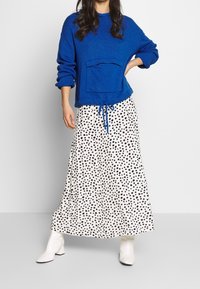 Blå stickad tröja med en framficka, kombinerad med en vit kjol med svarta prickar och vita ankelstövlar.