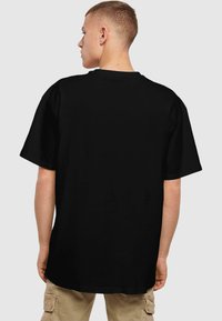 T-shirt noir en coton, avec une coupe décontractée, des manches courtes et un col rond. La vue arrière montre des coutures lisses et plates sans graphiques.