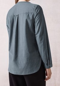 Camicia a maniche lunghe azzurro chiaro con piega centrale sul retro e polsini abbottonati, realizzata in un tessuto testurizzato, con scollatura rotonda e spacchi laterali.