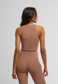 Smeđi rebrasti crop top s prilagođenim dizajnom, širokim trakama i nevidljivim rubom, u kombinaciji s odgovarajućim tajicama visokog struka.