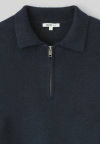 Pull en tricot bleu marine avec une fermeture éclair courte et un col. Texture douce avec une coupe ample. L'étiquette indique "BZX | L."